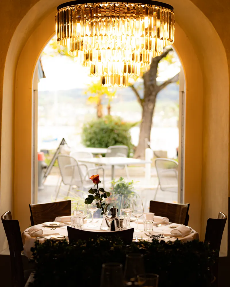 Speisesaal des LAGO: Kristallleuchter und gedeckter runder Tisch, durch den Rundbogen der Blick auf Terrasse und Zürichsee
