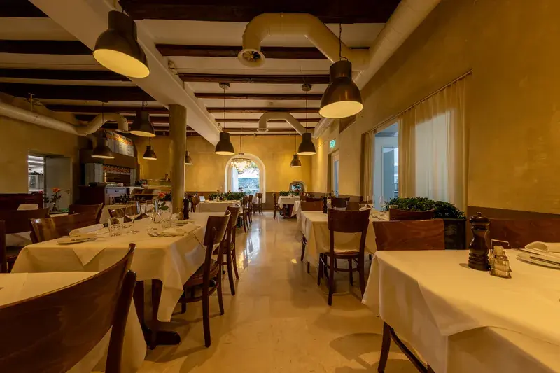 View through the LAGO dining room: wooden ceiling beams, pendant lamps and set tables