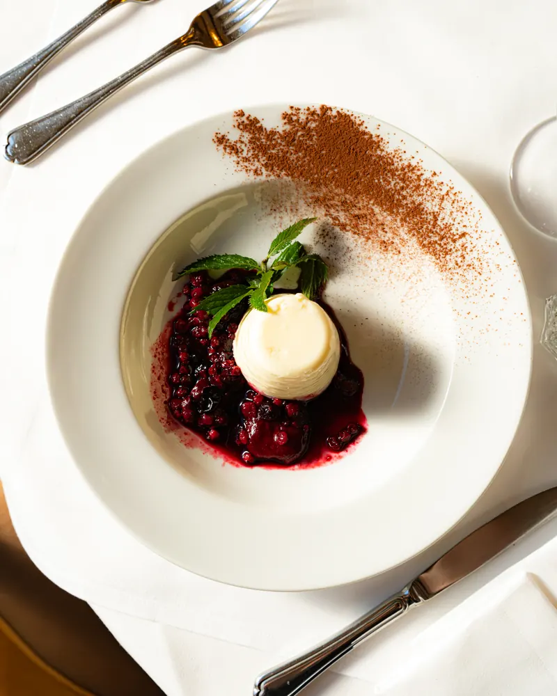 Panna Cotta mit warmen Beeren und Minze, Kakao auf dem Teller