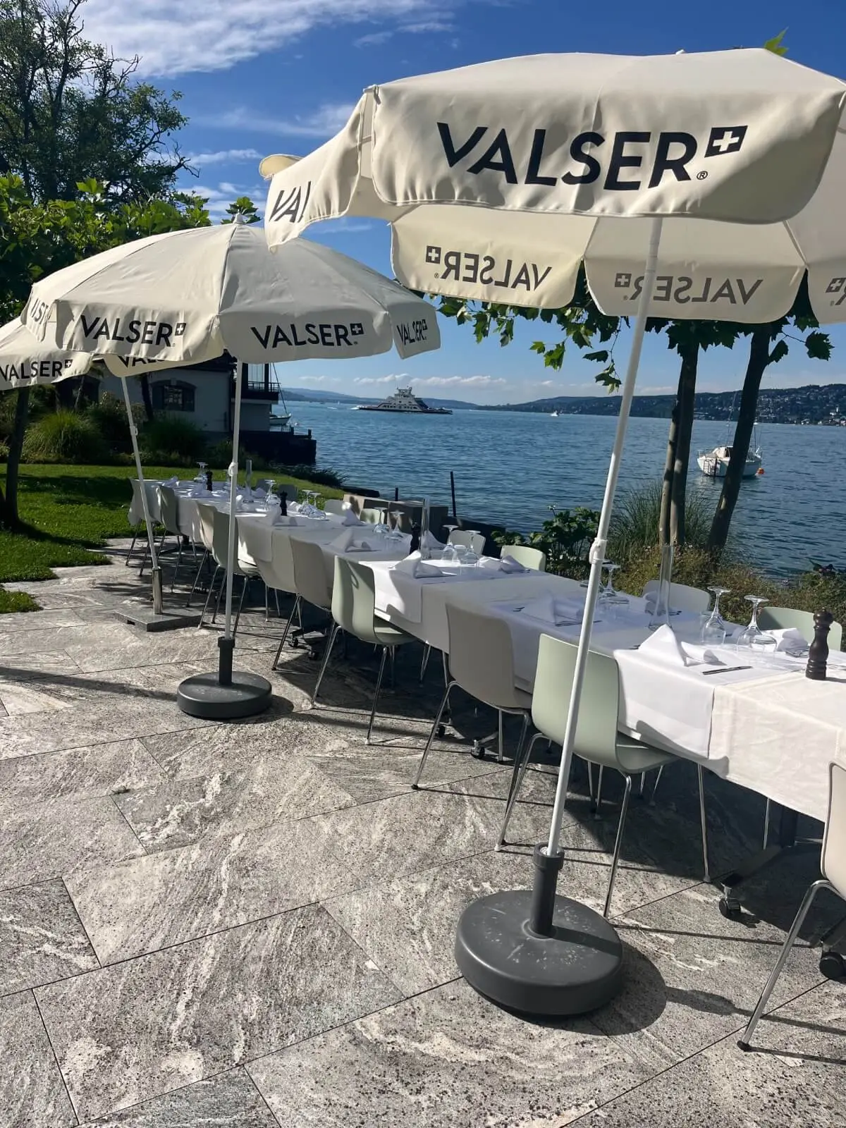 Lange Tafel unter cremefarbenen Schirmen auf der Seeterrasse