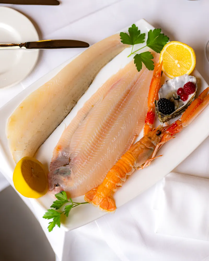 Seezungenfilets mit Langustine, Zitrone und Petersilie auf einer weissen Platte